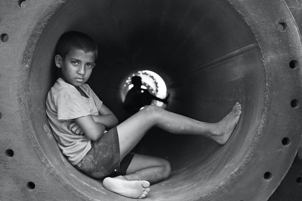 grayscale photo of boy in crew neck t shirt sitting in round pipe