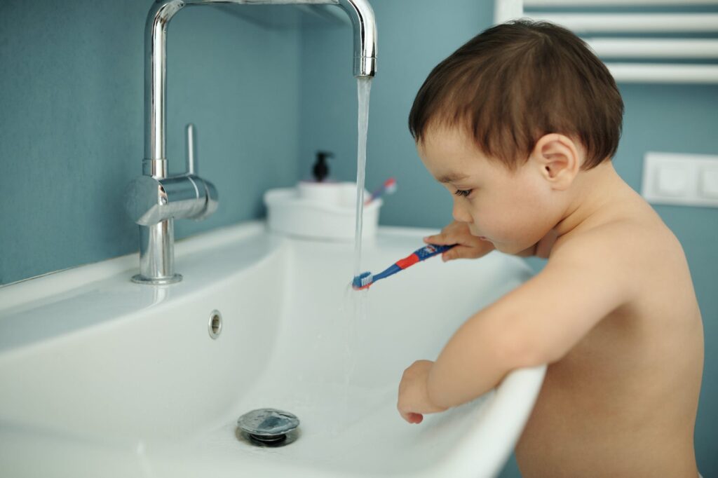 a kid washing the toothbrush under the faucet